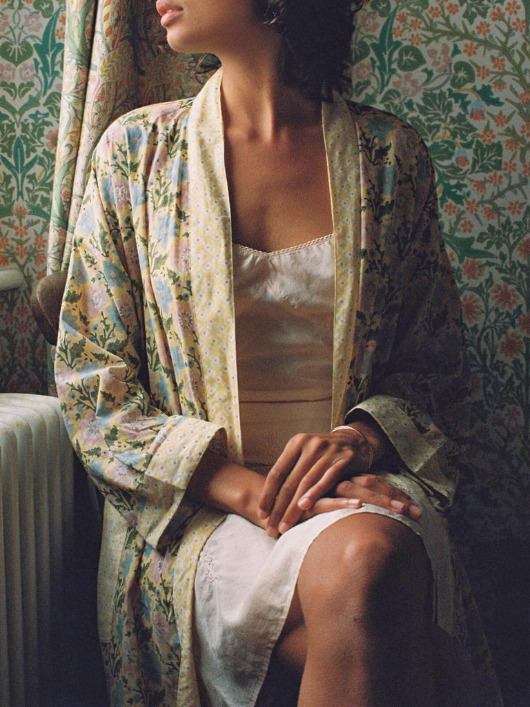 Model sitting at a window wearing a floral block print robe in buttermilk and a delicate slip dress.