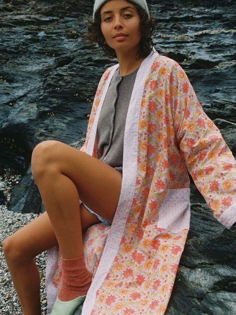 Model wearing a floral lilac block print robe, cosy knit and hat on a pebble beach.