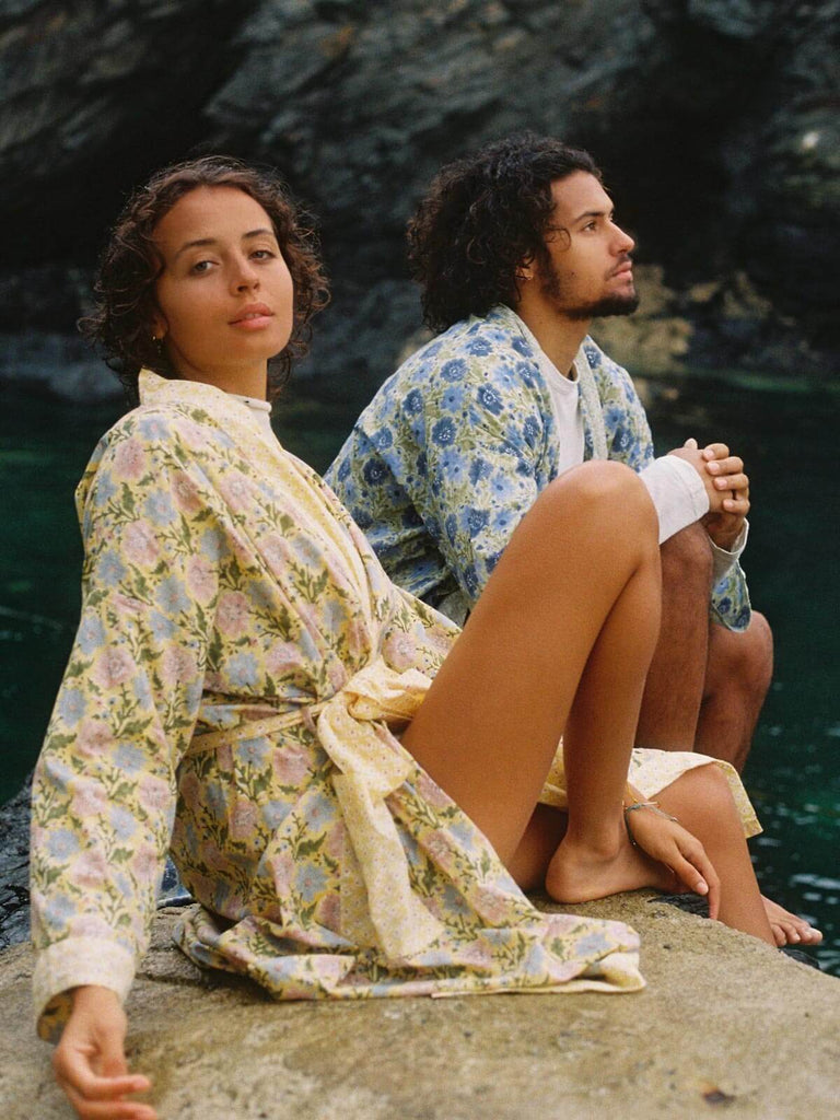 A male and female model wearing block print floral robes by the sea