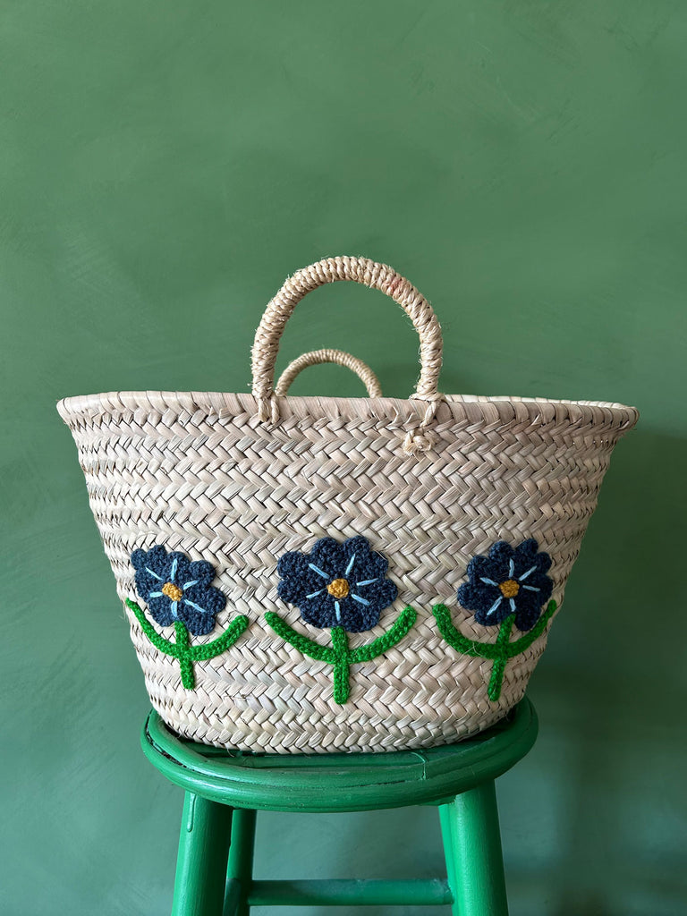 Close-up of a hand-embroidered market basket with daisies, set on a green stool against a vibrant green wall by BohemiaDesign