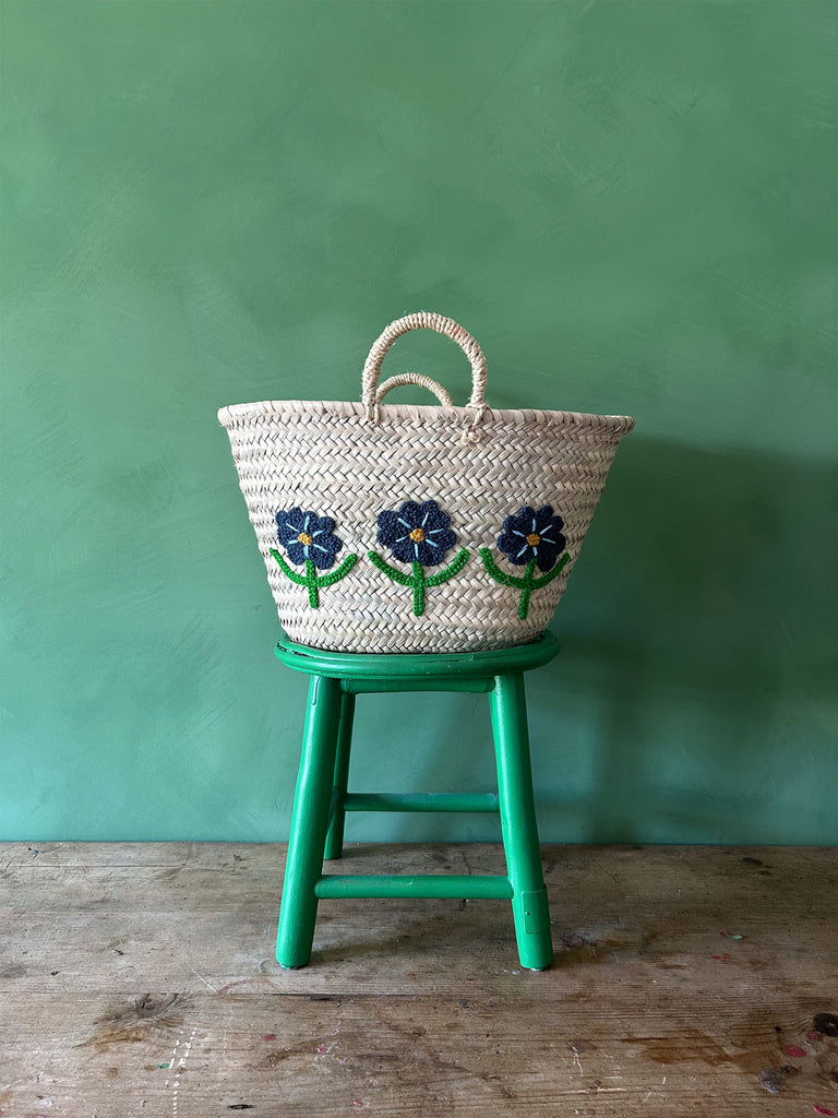 Hand-embroidered market basket adorned with daisies, set on a green stool against a vibrant green wall | Bohemia Design