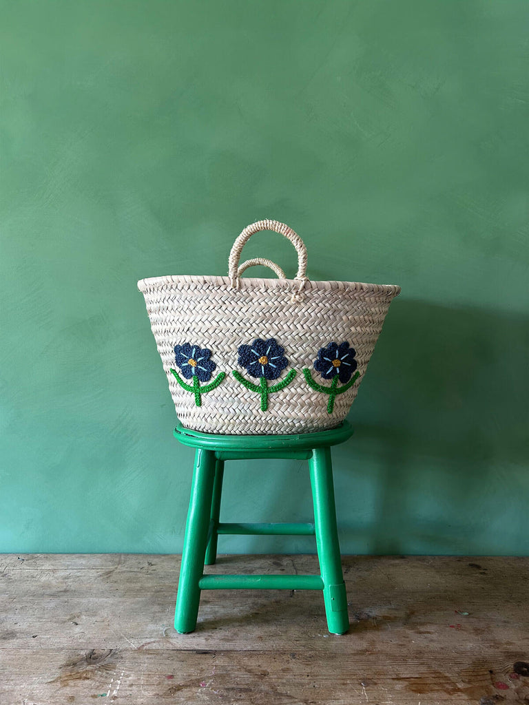 Hand-embroidered market basket adorned with daisies, set on a green stool against a vibrant green wall | Bohemia Design