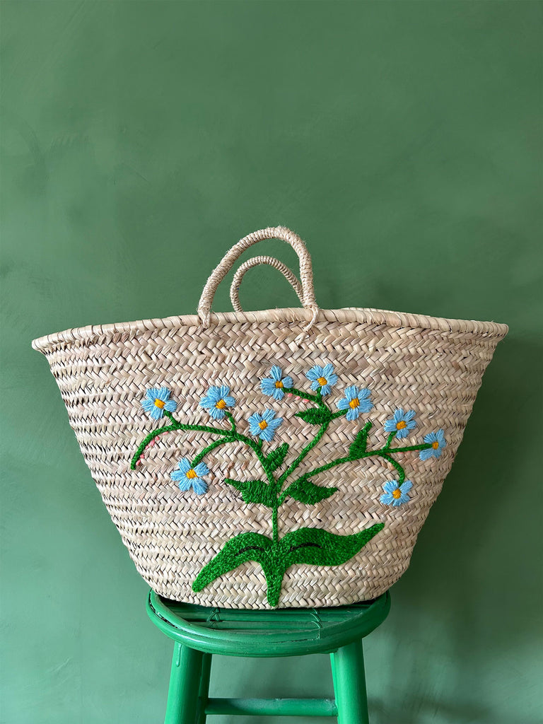 Natural basket with a hand-embroidered blue flowers on a green stool against a green wall | Bohemia Design