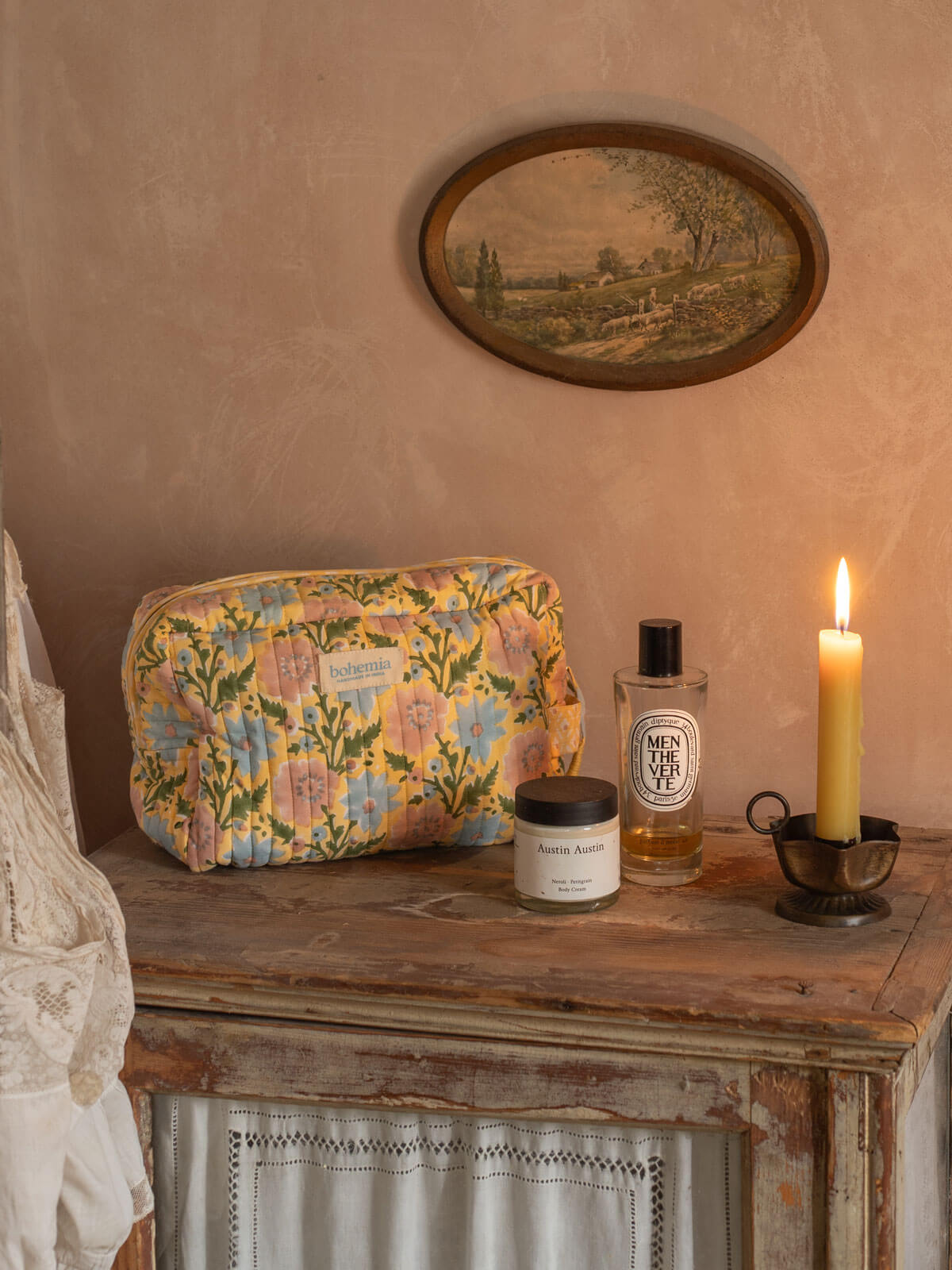 A Floribunda washbag in buttermilk yellow on a antique dresser alongside perfume bottles and a lit candle