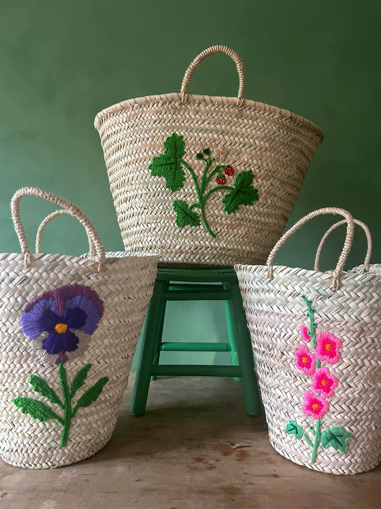 A group of natural hand-woven Moroccan baskets featuring three new exquisite hand-embroidered botanical and floral designs by BohemiaDesign