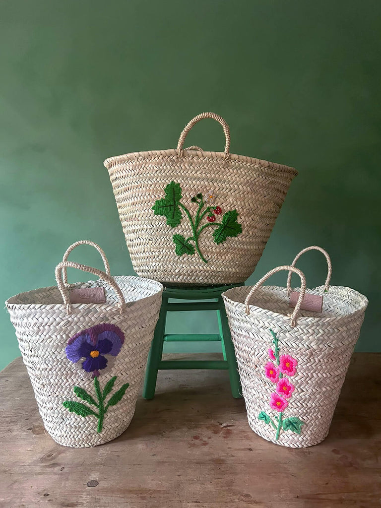 A group of natural hand-woven Moroccan baskets featuring three new exquisite hand-embroidered botanical and floral designs  by BohemiaDesign