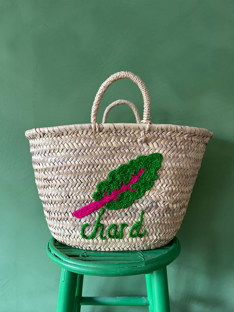 Close-up of a natural basket bag with short handles, featuring a hand-embroidered illustration of chard and text | Bohemia Design