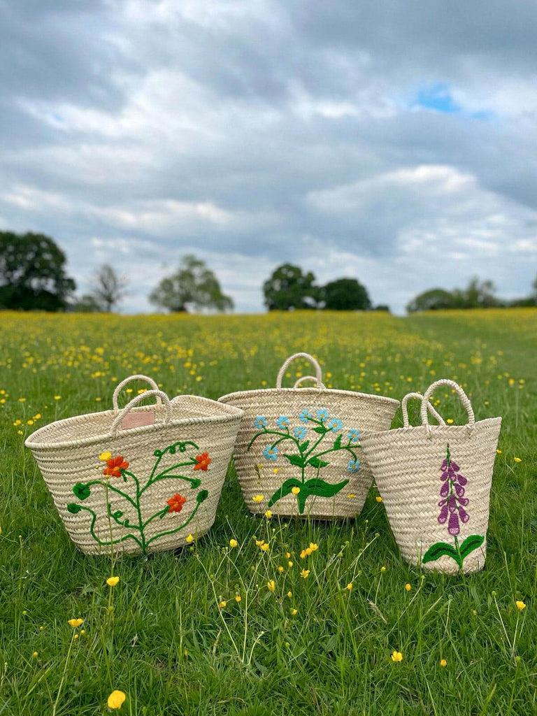 Hand-embroidered tote basket bags in three unique floral designs, displayed on a green meadow with yellow flowers by Bohemia Design