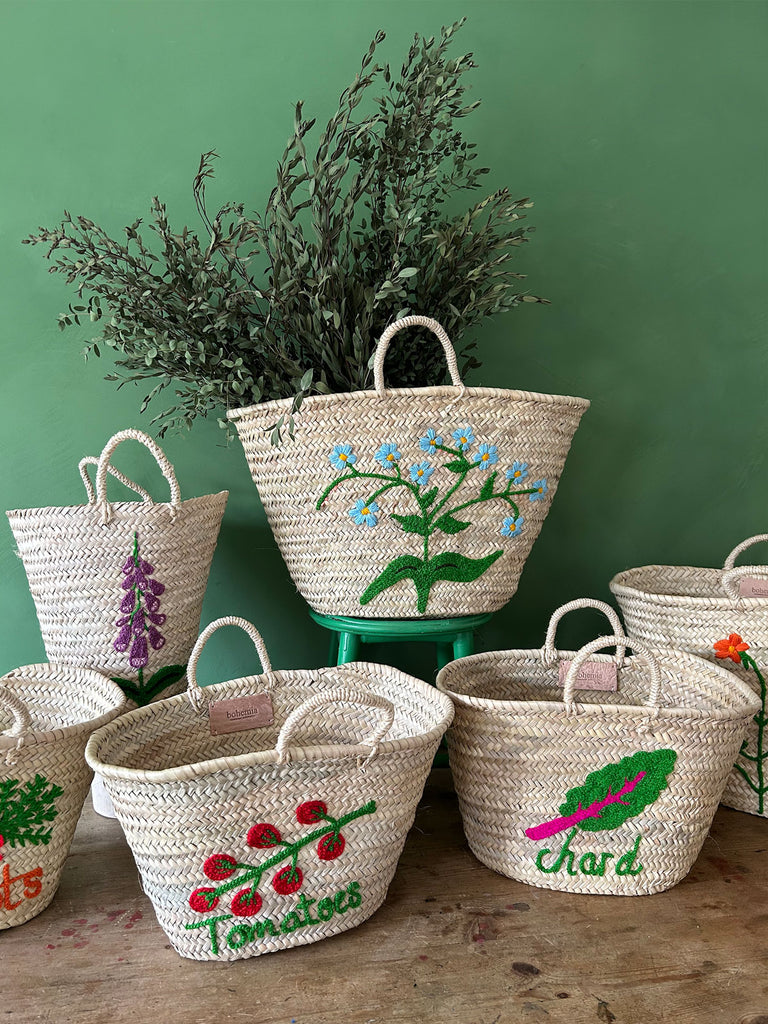 A group of natural, hand-embroidered baskets set against a lush green wall, curated by Bohemia Design