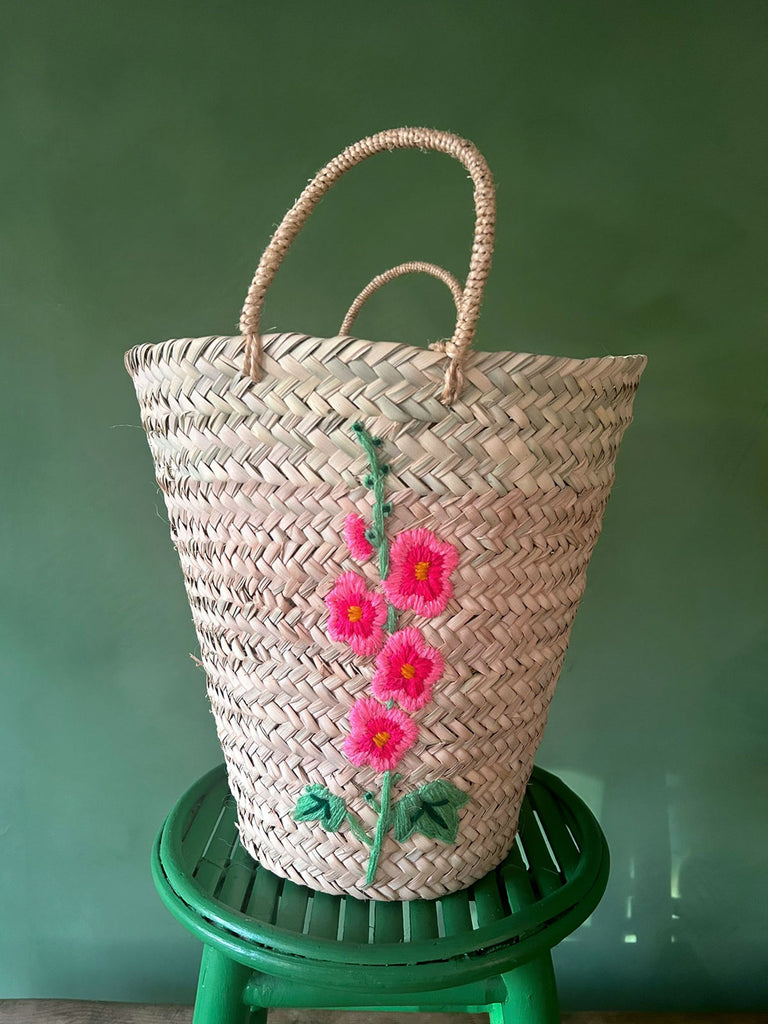 A close-up view of a embroidered pink hollyhock flower, intricately hand stitched onto a bucket-shaped basket | Bohemia Design Wholesale