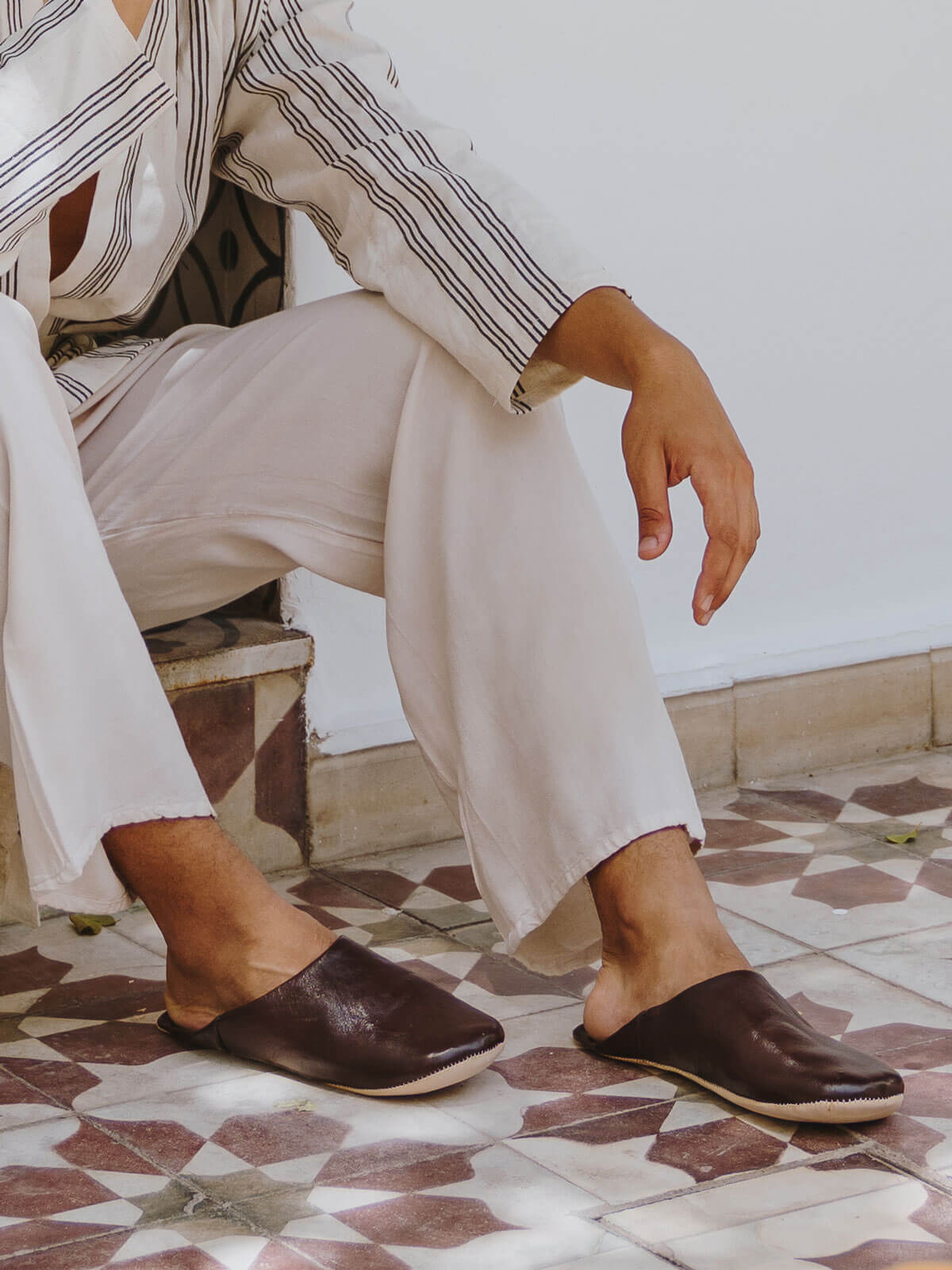 A man in linen trousers wearing a pair of brown leather babouche slippers 