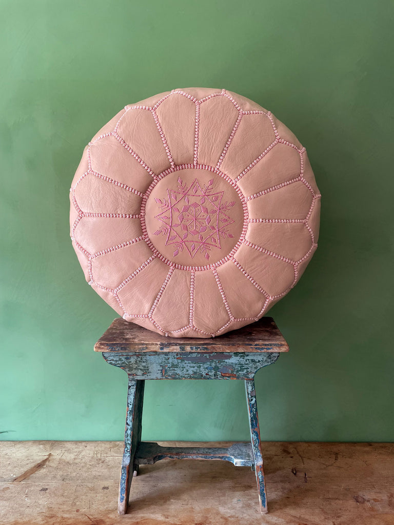 Authentic Moroccan leather pouffe in ballet pink, placed on a stool against a green wall by Bohemia Design