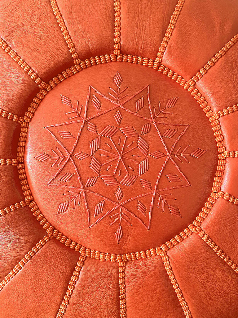 A close-up shot of a hand-embroidered star design on a deep orange Moroccan leather pouffe | Bohemia