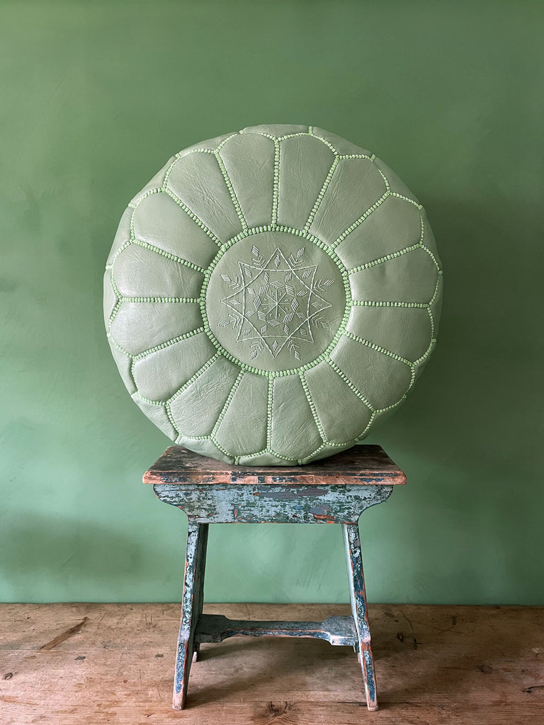 Authentic Moroccan leather pouffe in sage, placed on a stool against a green wall by Bohemia Design