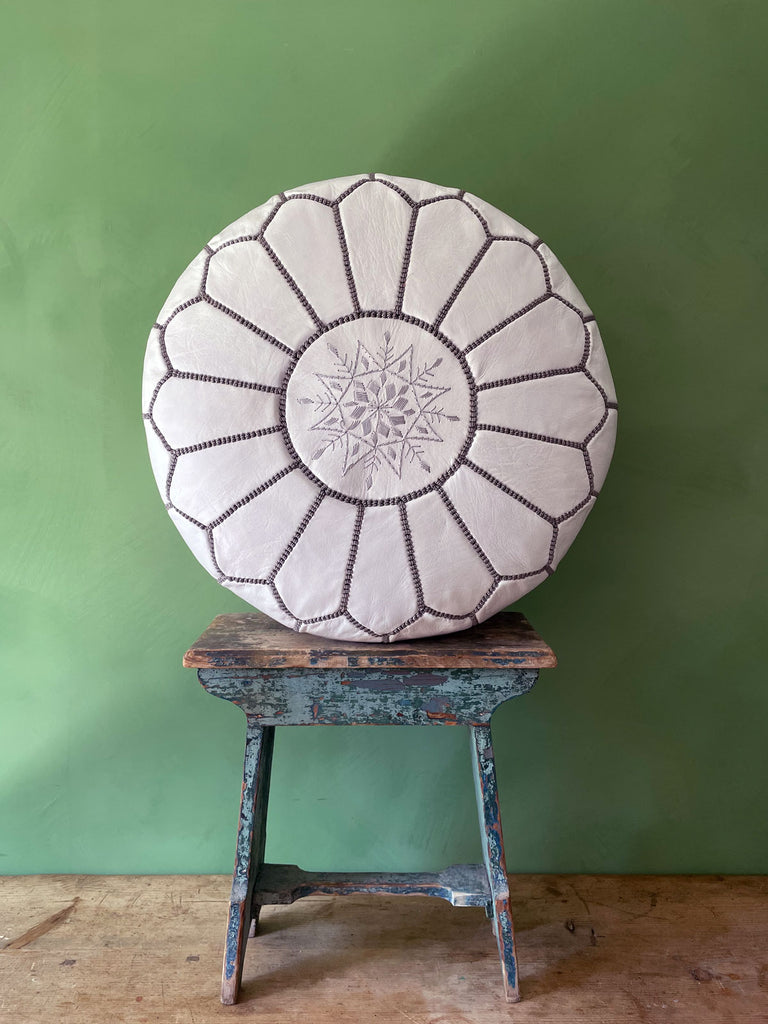 Authentic Moroccan leather pouffe in white and grey, placed on a stool against a green wall by Bohemia Design