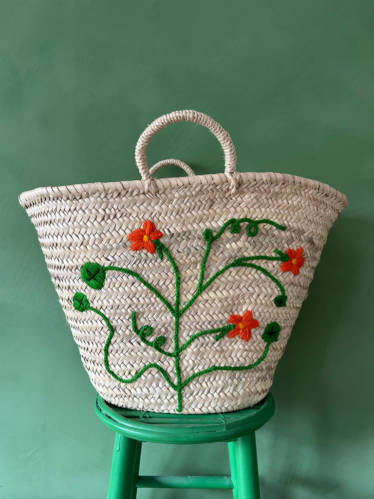 Natural woven basket bag with hand-embroidered nasturtium floral motif on a green stool against a green wall | Bohemia Design