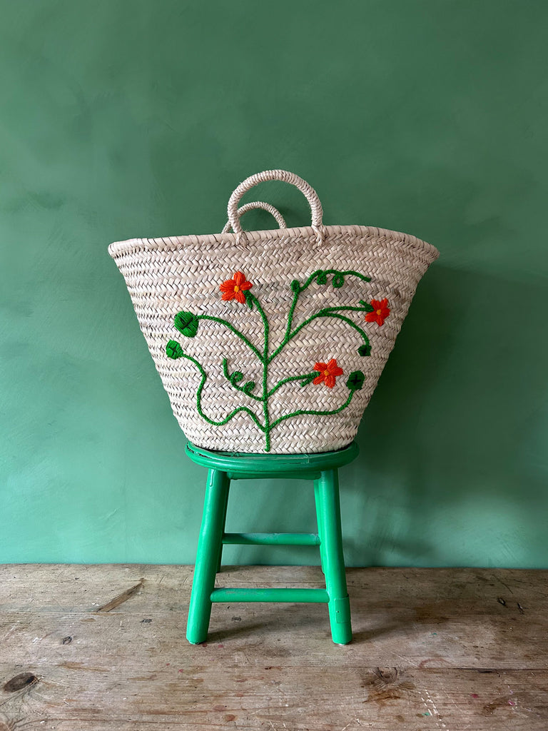 Handwoven market basket bag with vibrant hand embroidered nasturtium florets on a green stool against a green wall | Bohemia Design