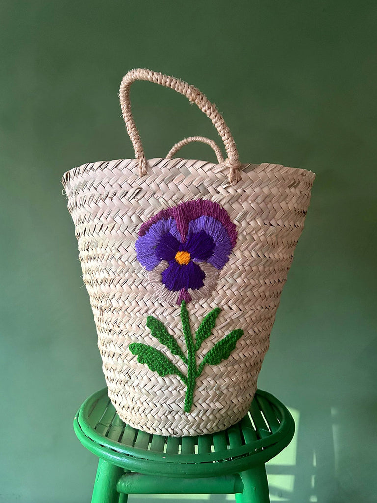 A close-up view of a hand-embroidered pansy flower, intricately stitched onto a bucket-shaped basket by BohemiaDesign