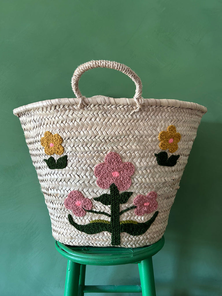 A close-up of a hand-embroidered market basket with our posy floral design on a green background | Bohemia Design