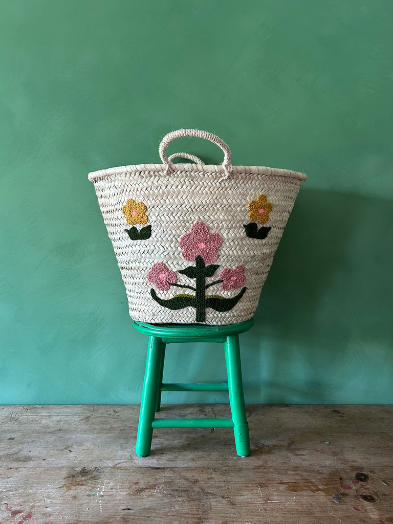 Hand embroidered market basket with two short handles, featuring our posy floral design, set against a vibrant green wall by Bohemia