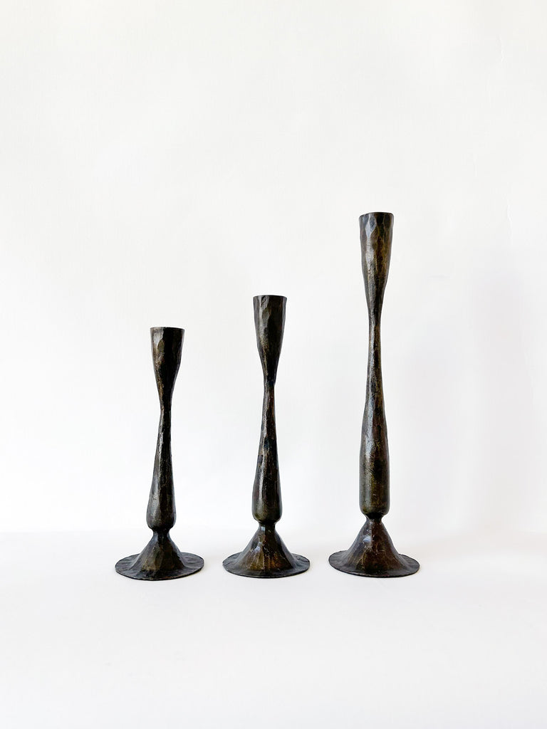 Three antique iron candle holders in varying sizes on a white background