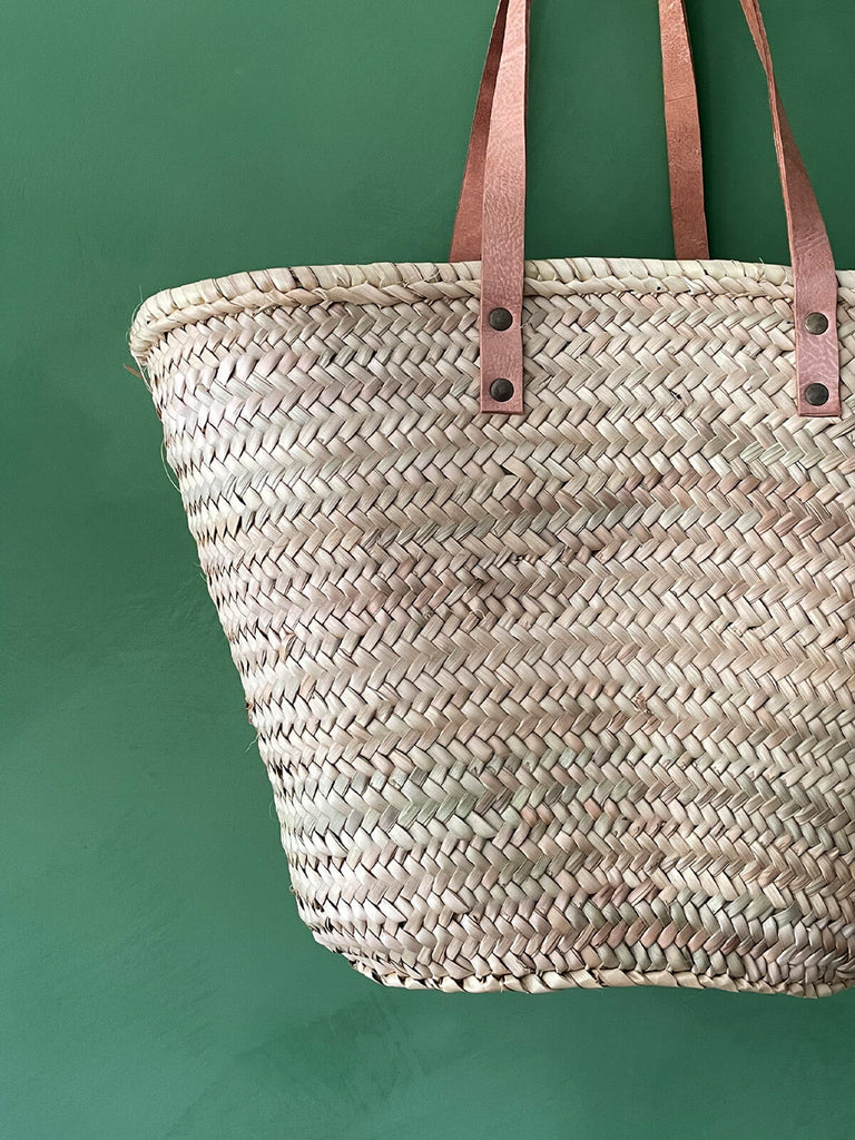 A close-up of a handwoven natural straw basket bag with flat leather shoulder straps | Bohemia Design