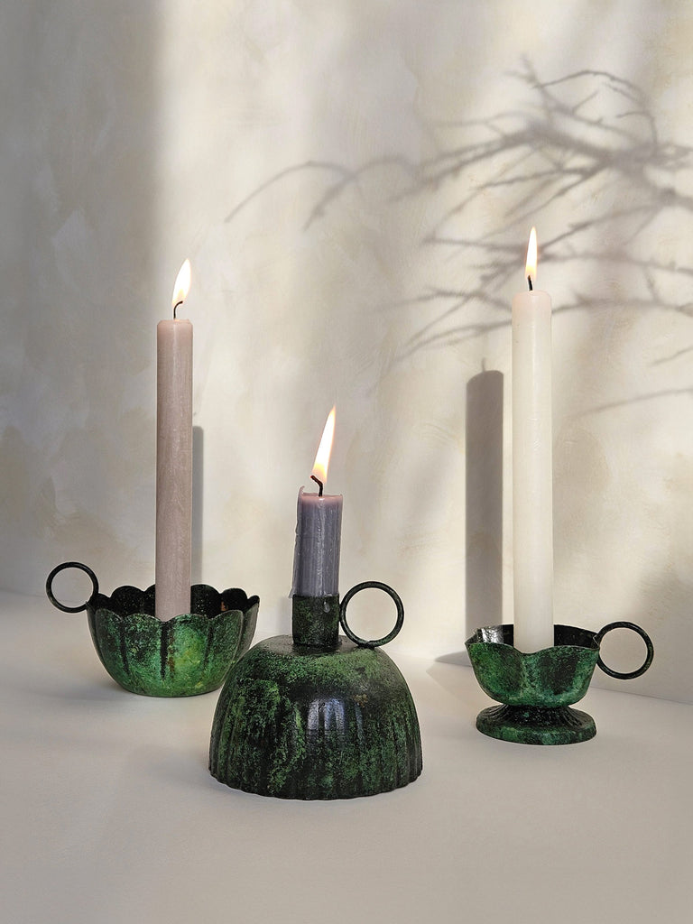 Iron candle holders with a vintage moss patina finish, paired with lit candles casting soft shadows on a slightly textured background | Bohemia