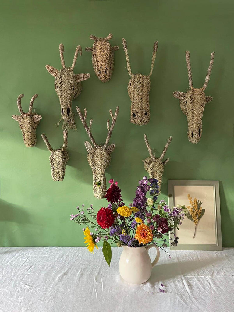 A group of natural woven wall mounted animal heads on a green wall