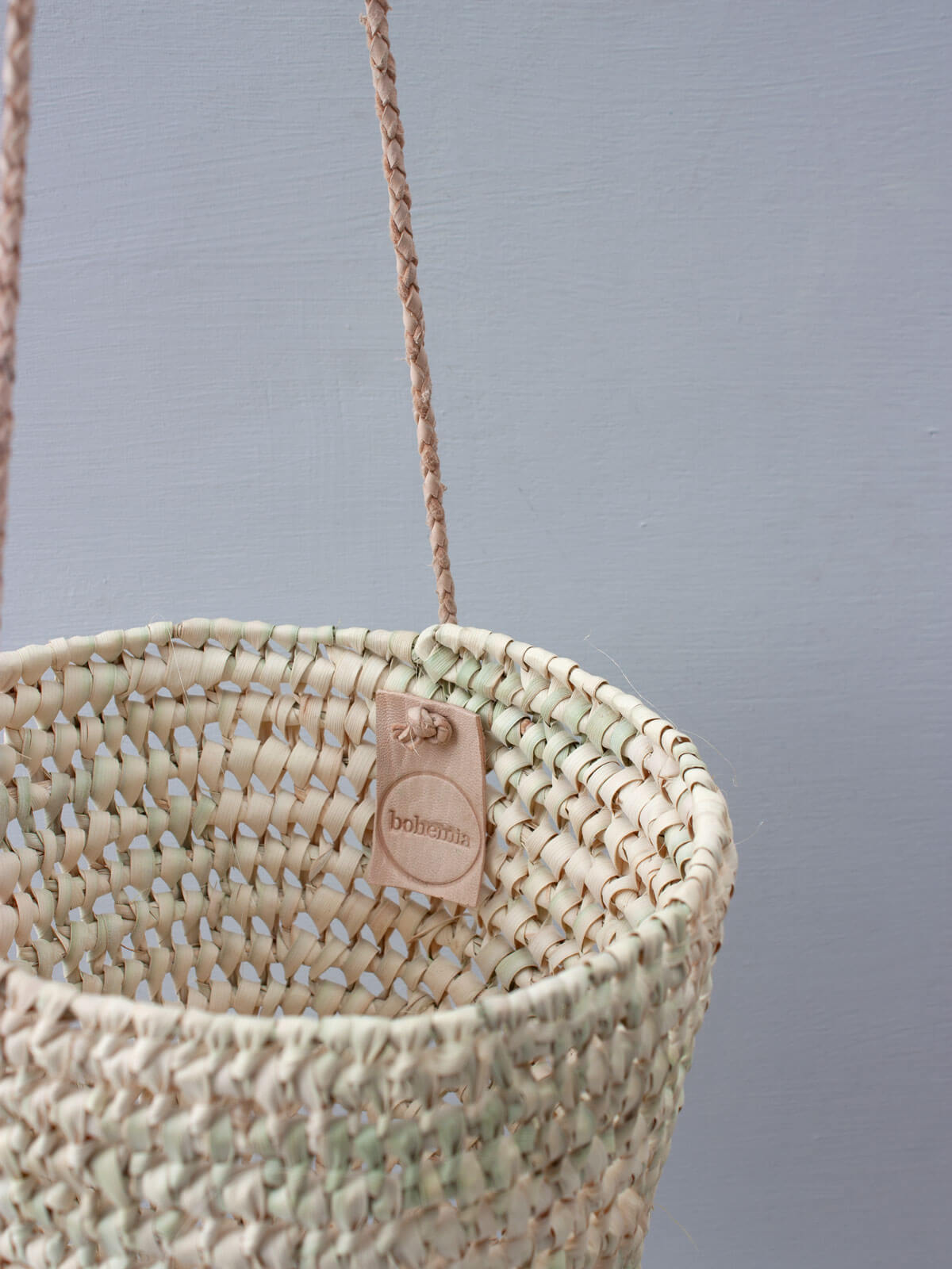 A natural woven indoor hanging basket with finely braided leather thongs and hand stamped Bohemia label inside